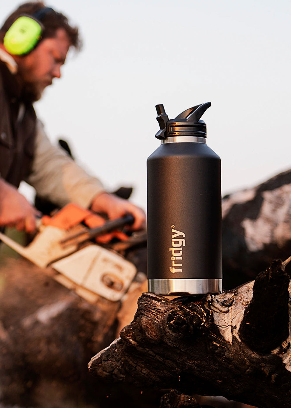 Fridgy All-Dayer Bottle in Black placed in front of a man using a chainsaw – Triple-wall insulated stainless steel water bottle designed for all-day hydration in rugged conditions.