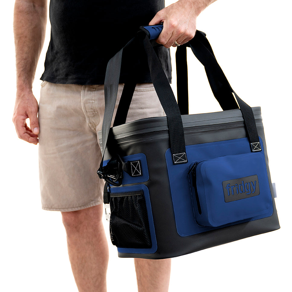 Person holding a blue 20L Fridgy Weekender cooler bag on a white background