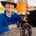 Person holding an orange Fridgy Mini Sipper tumbler with a horse in the background