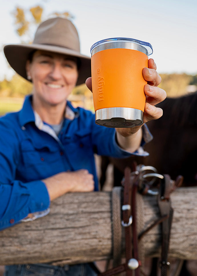 Person holding an orange Fridgy Mini Sipper tumbler with a horse in the background