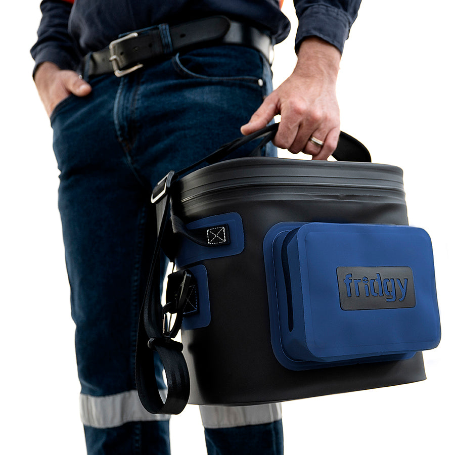 Person holding a blue 8L Fridgy Cribmate cooler bag on a white background