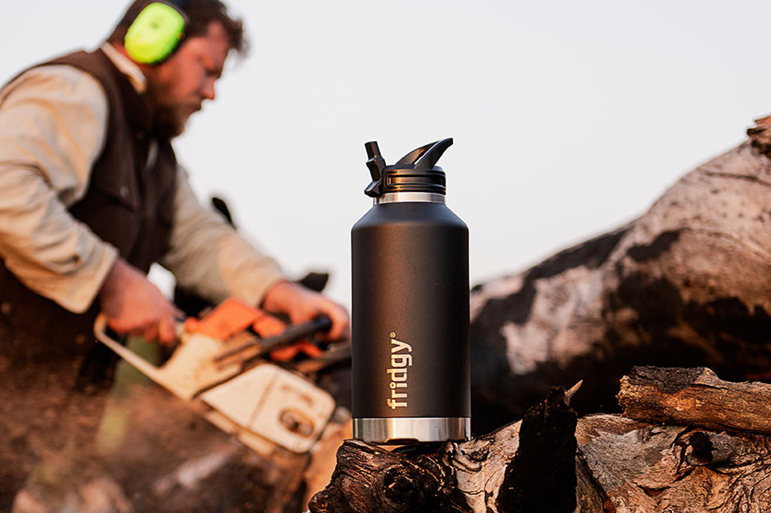 Fridgy 1.9L All-Dayer Bottle – Triple-wall insulated stainless steel water bottle placed in front of a man working hard with a chainsaw, built for all-day hydration in rugged conditions.