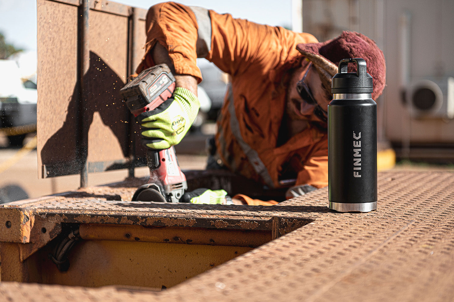 Fridgy Grip Range Bottle – Triple-wall insulated stainless steel water bottle placed in front of a worker using a grinder, built for durability and all-day hydration in tough conditions.