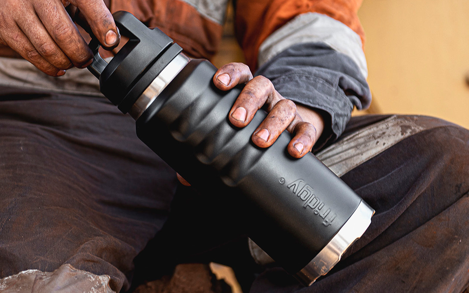 Fridgy 1080ml Grip Range Bottle in Dark Hour Black held in a dirty tradie's hand – Triple-wall insulated stainless steel water bottle built for durability and all-day hydration on the job site.