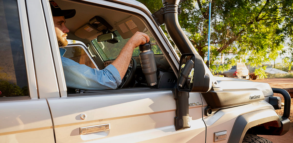 A Fridgy Cruise Range insulated bottle in the door of a ute while the driver is behind the wheel.