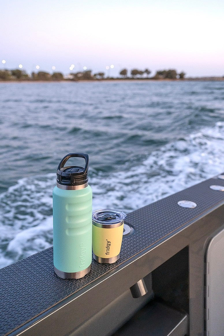 Fridgy 1080ml Grip Range Bottle and Mini Sipper Tumbler – Double-wall vacuum insulated water bottle and double-wall insulated tumbler placed on the edge of a boat, designed for hot and cold drinks on the water.