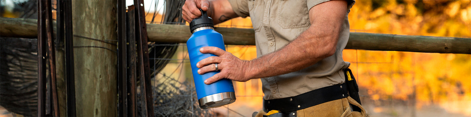 Tradie holding Fridgy 1.9L All-Dayer Bottle in Regal Blue with a rural farm backdrop – Built-tough hydration gear for job sites and off-grid work.