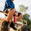 Child sitting on a vehicle holding a red 780ml Fridgy Grip Range bottle with trees in the background