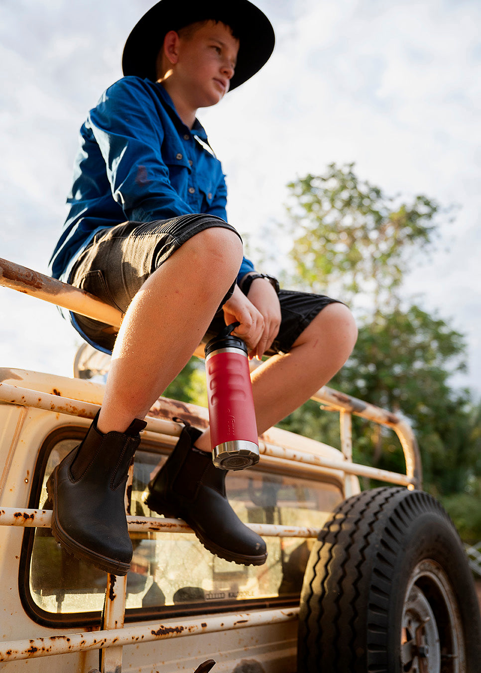 Child sitting on a vehicle holding a red 780ml Fridgy Grip Range bottle with trees in the background