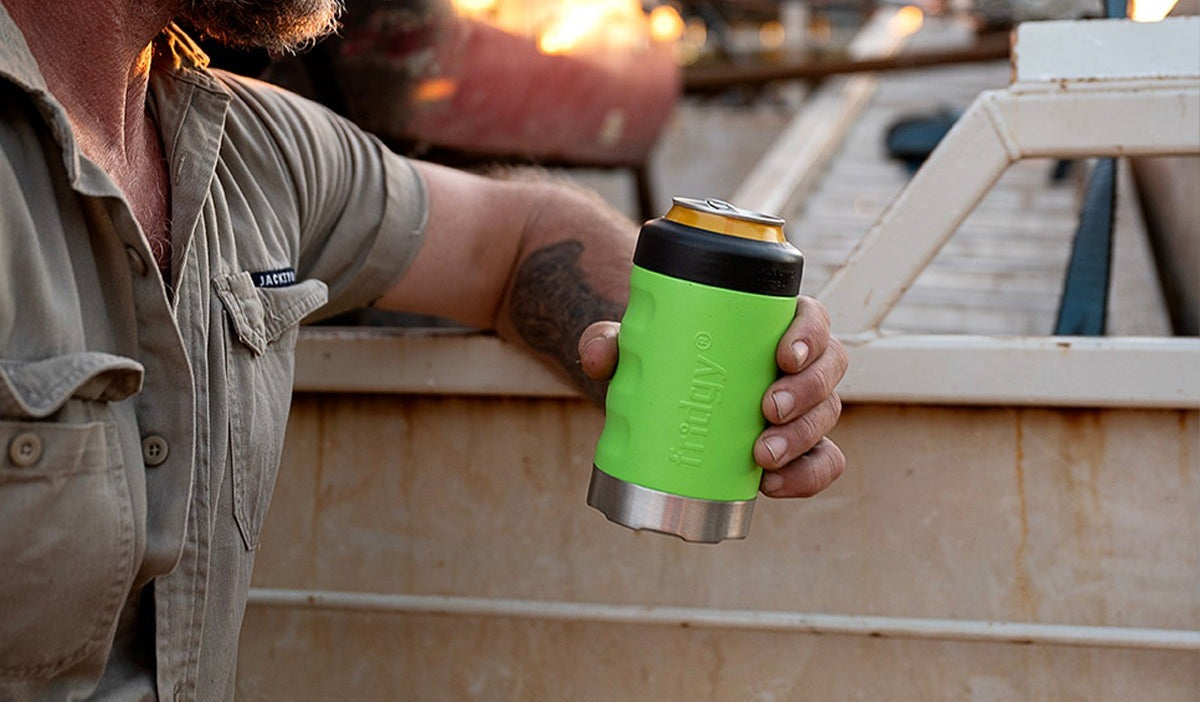 A tradie holding a nitro green Fridgy can cooler on the tray of a ute at sunset.